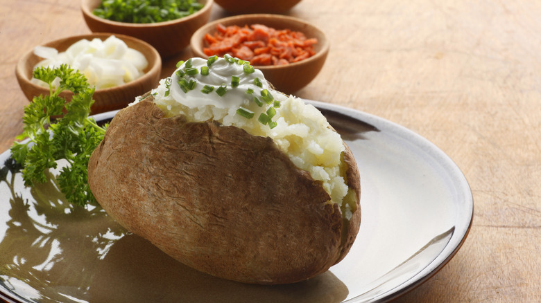 Plated baked potato with bowls of toppings