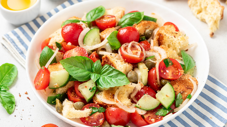 A bowl of panzanella salad filled with cherry tomatoes, croutons, basil, and red onion slices