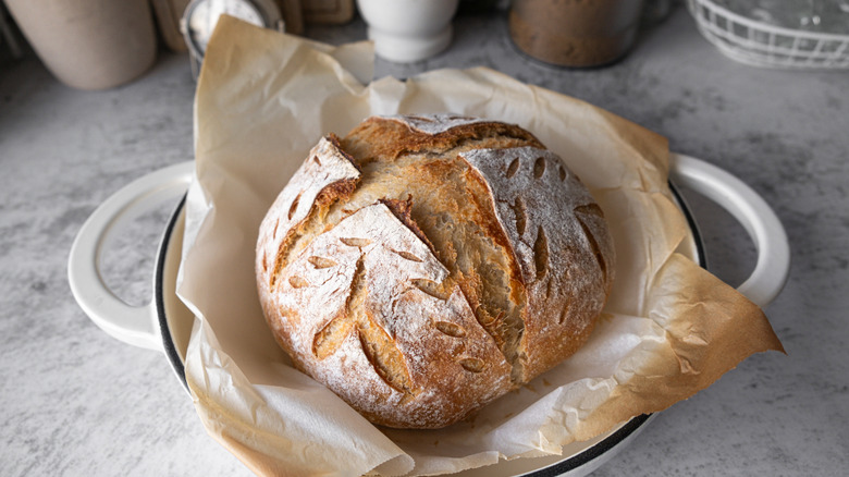 A loaf of round sourdough bread in a paper lined Bowl