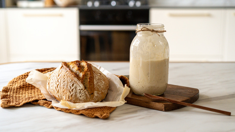 Sourdough starter in a jar with a bread loaf