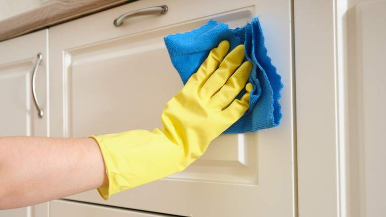 A woman washes furniture in her home kitchen with a blue cloth