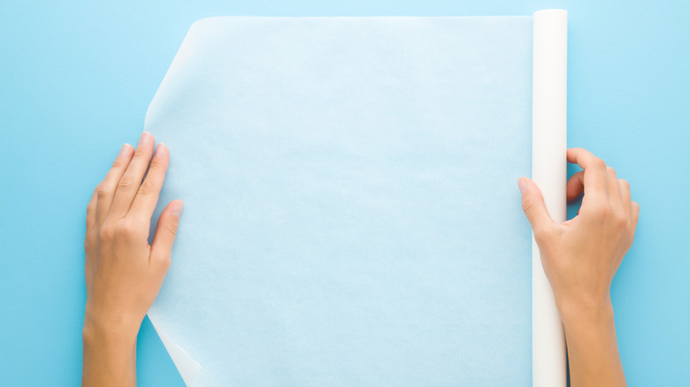 Hands unrolling parchment paper on a kitchen counter
