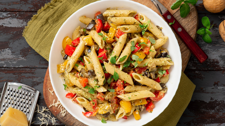 a bowl of pasta salad with cheese, tomato, peppers, and eggplant
