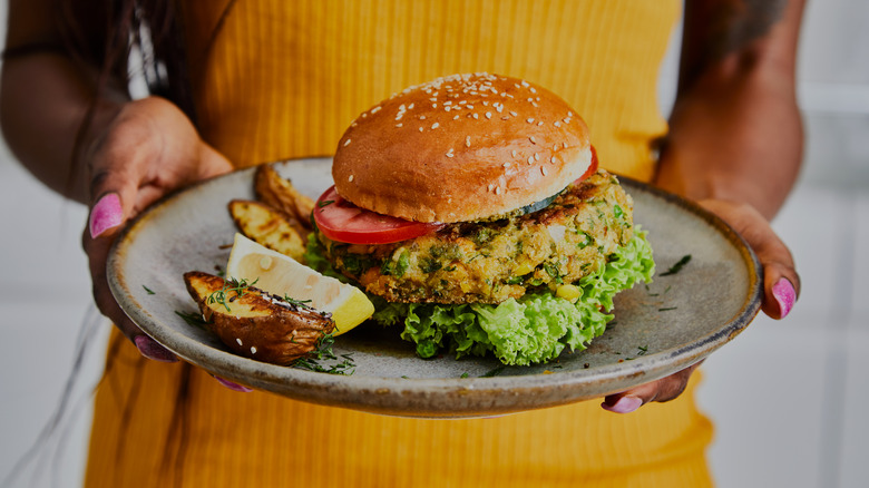 woman holding veggie burger on plate