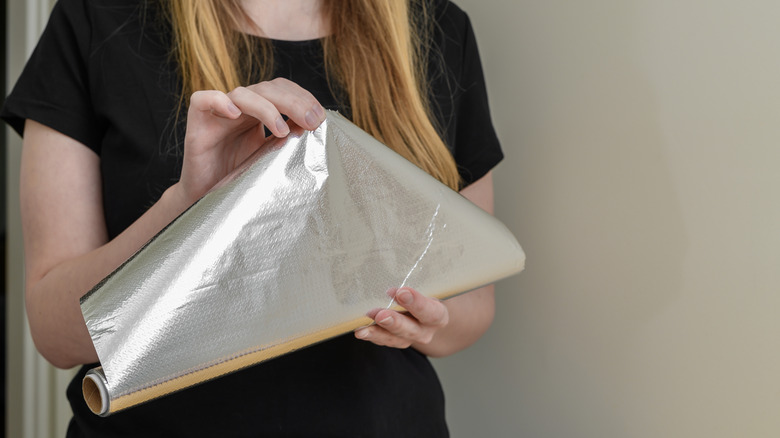 A person peels a sheet of aluminum foil off of a roll