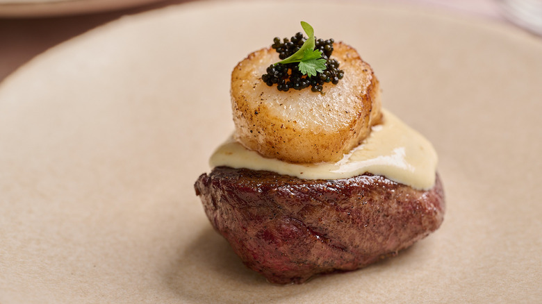 steak, sauce, and scallop stacked on a plate