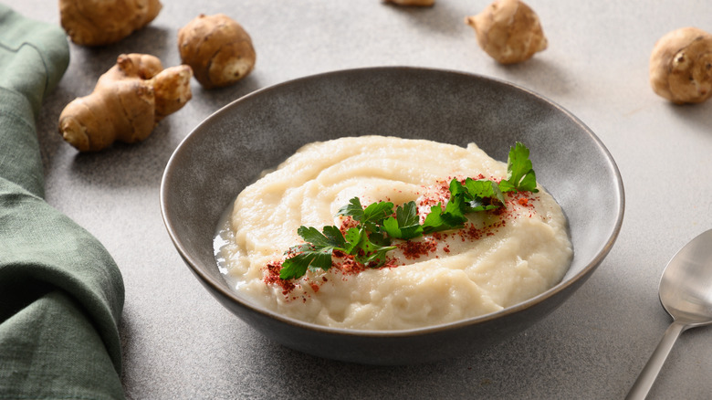 Mashed sunchokes in a bowl with raw sunchokes in the background