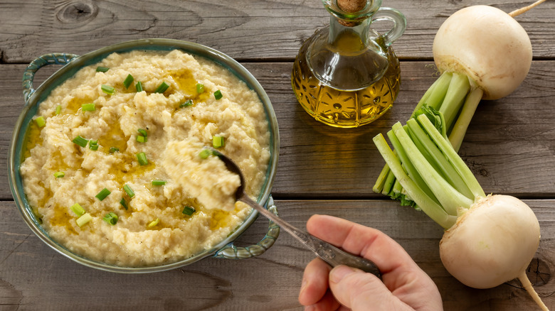 Mashed turnip mashed with a hand adding ingredients