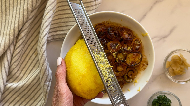hand zesting lemon over bowl
