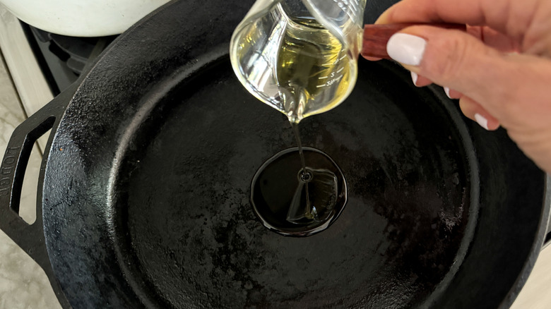 hand adding oil to skillet