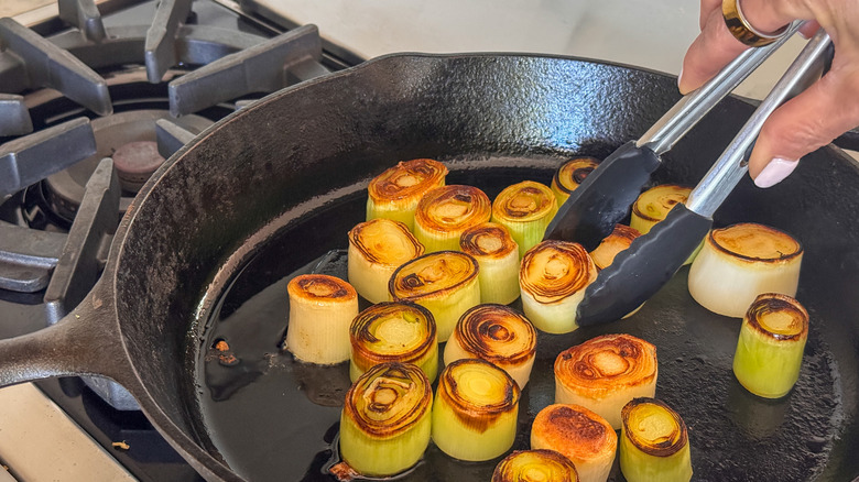 hand flipping leeks in skillet