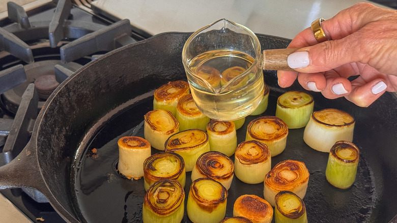 hand adding wine to pan with leeks
