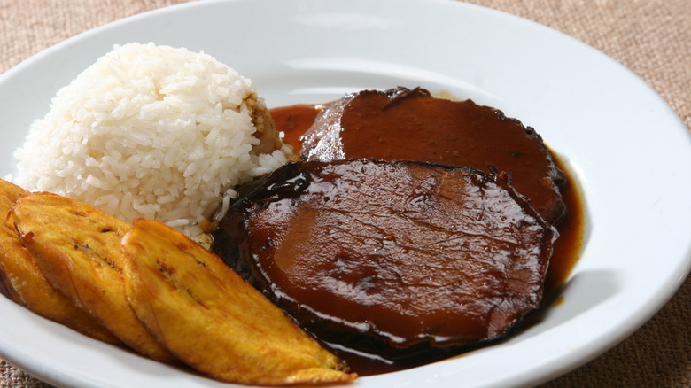 Bowl of Venezuelan asado negro, made with braised round roast, white rice, and fried plantains