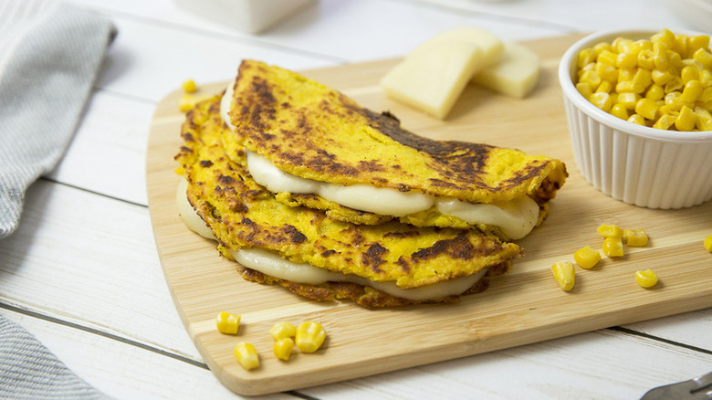 Venezuelan cachapas (cheese-filled corn pancakes) on a wooden board with a bowl of corn