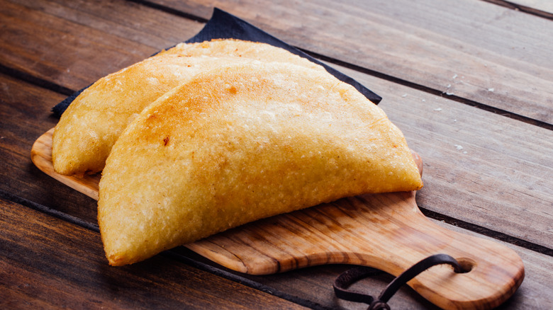 Two empanadas on a wooden serving board