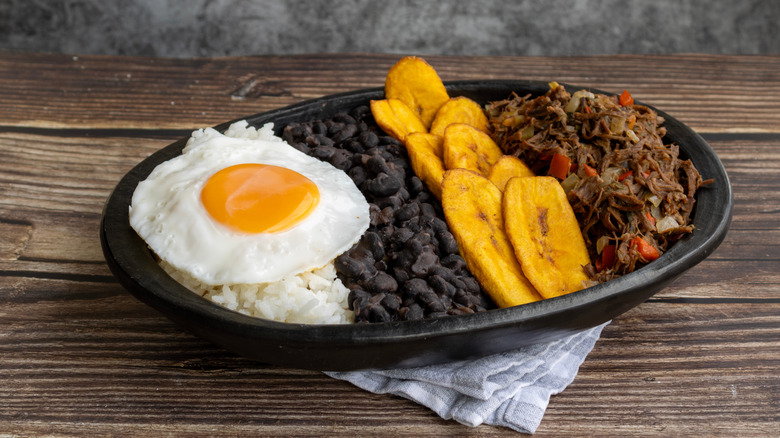Plate of Venezuelan pabellón criollo, with black beans, plantains, shredded beef, and a fried egg