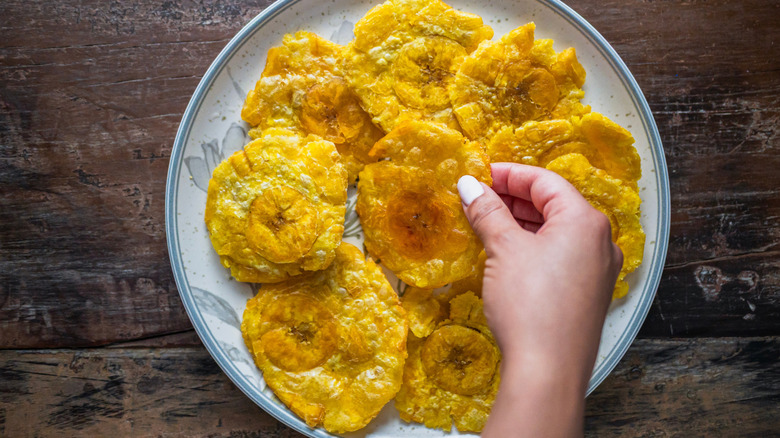 Patacones (crispy smashed and fried plantains) on a plate, with a hand picking one up