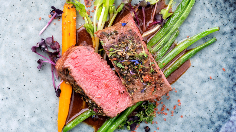 A dressed plate of sliced venison backstrap with bright vegetables