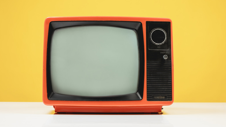 Old retro red TV on white table with blank screen on yellow background
