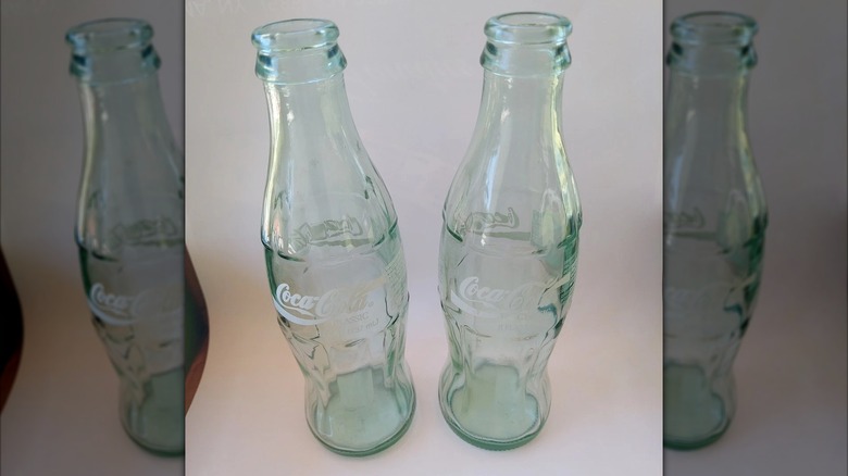 two empty glass coca-cola bottles against white background