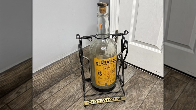 Old Taylor Bourbon Whiskey Bottle in vintage pourer on floor against door