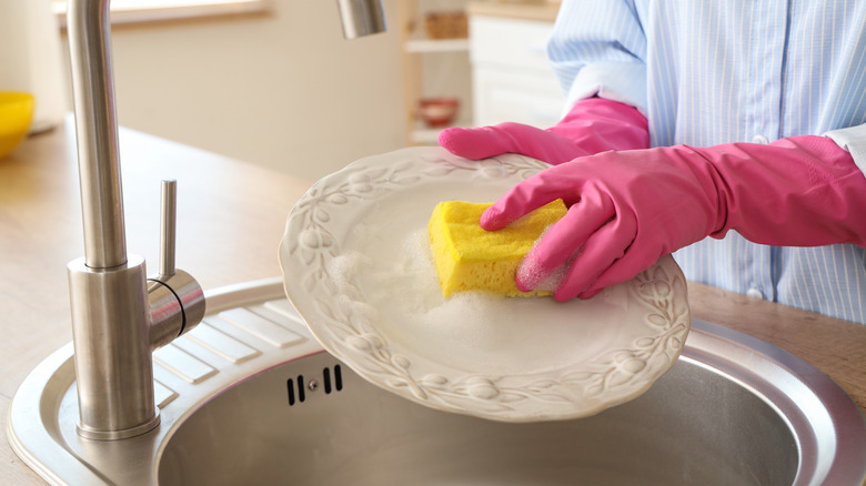 Gloved hands washing a vintage plate in the sink