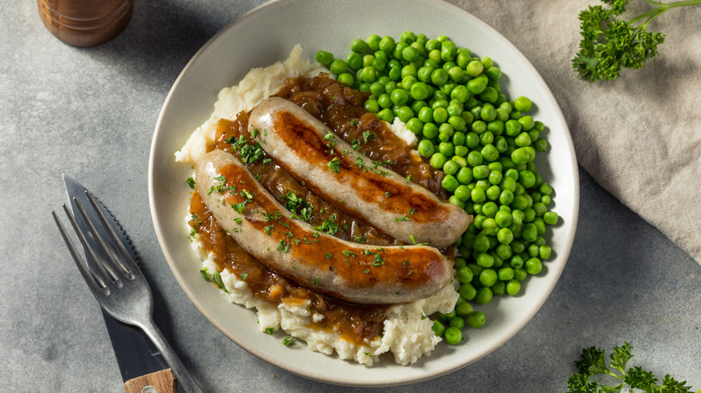 White plate with bangers and mash and peas viewed from above