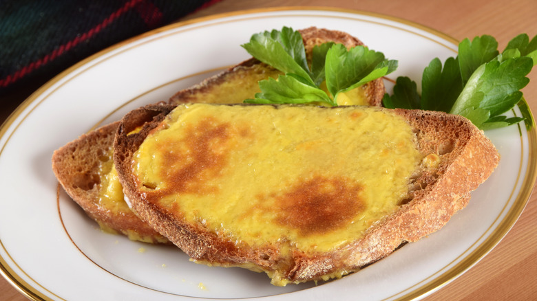 Welsh rarebit and garnishes on a white plate with a gold rim