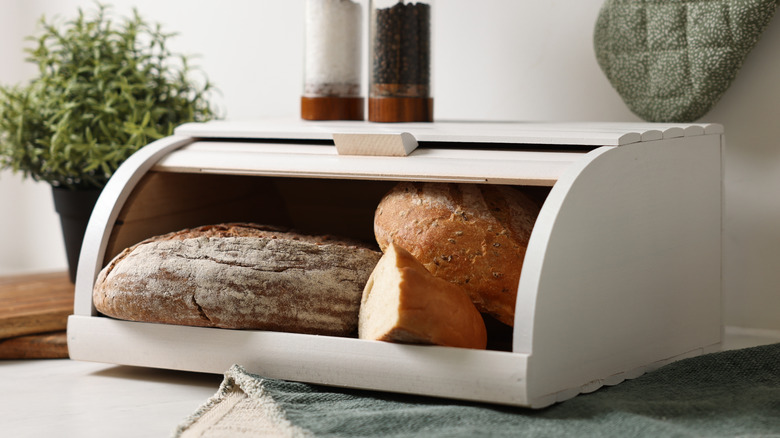 Wooden, white bread box that's open and displaying three loaves of bread.
