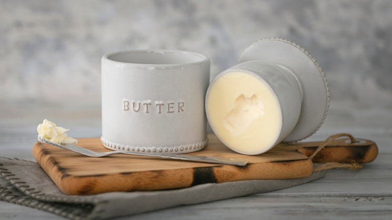 An open ceramic butter bell, with a tiny chunk of butter missing, taken out with a serving knife.
