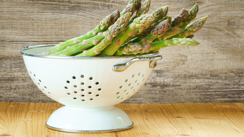 A bunch of fresh asparagus in a white enameled colander.