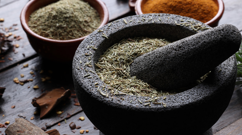 Large stone-made mortar and pestle, filled with dry herbs.