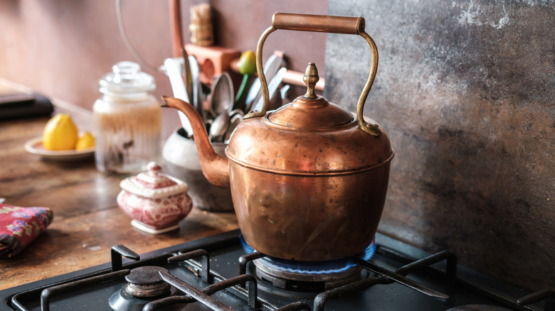 Copper tea kettle on a turned on gas burner.