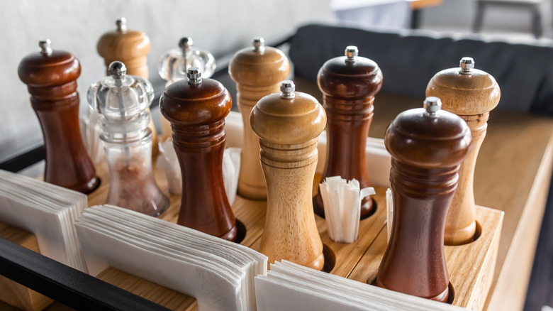 Wooden salt and pepper mills in light and dark shades, in a restaurant setting.