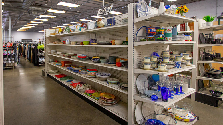 Kitchen items on the shelves of a thrift store including plates and cups