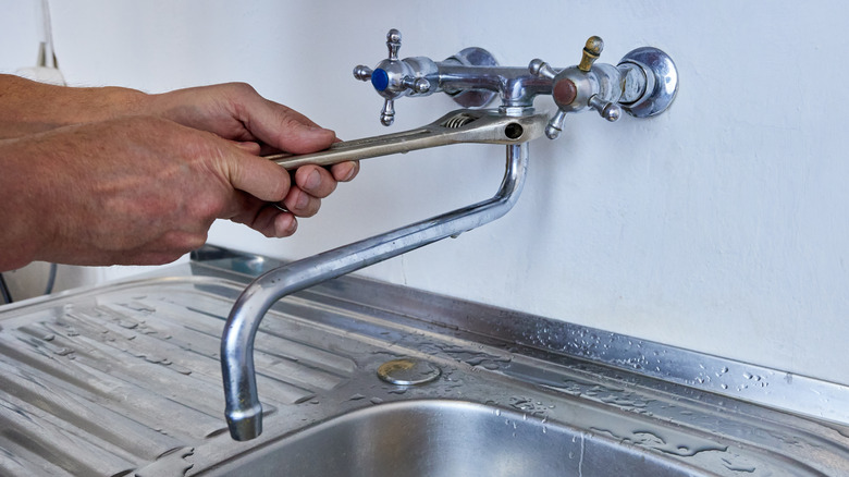 Man tightens spout on silver wall mounted faucet with wrench