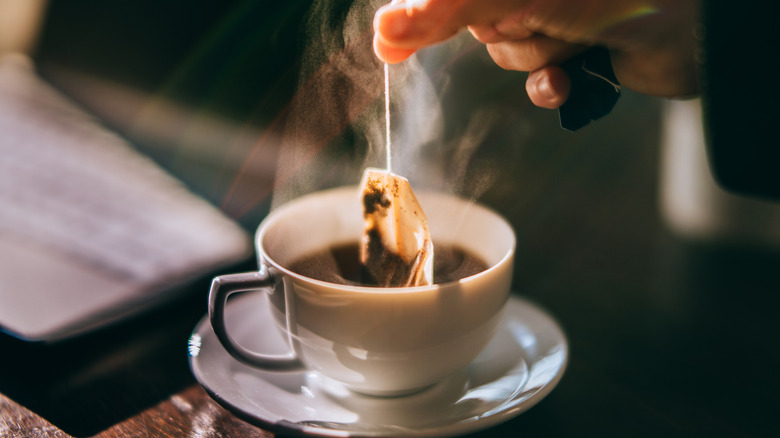 Someone dipping a teabag into a small, white mug
