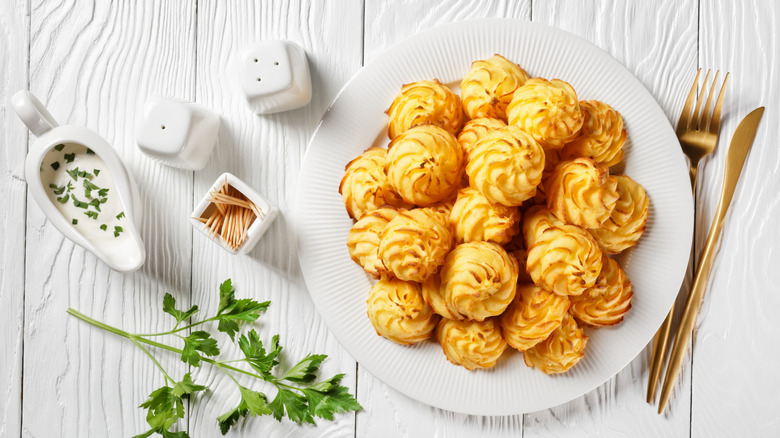Duchess potatoes served with white sauce on a white plate on a wooden table with golden cutlery