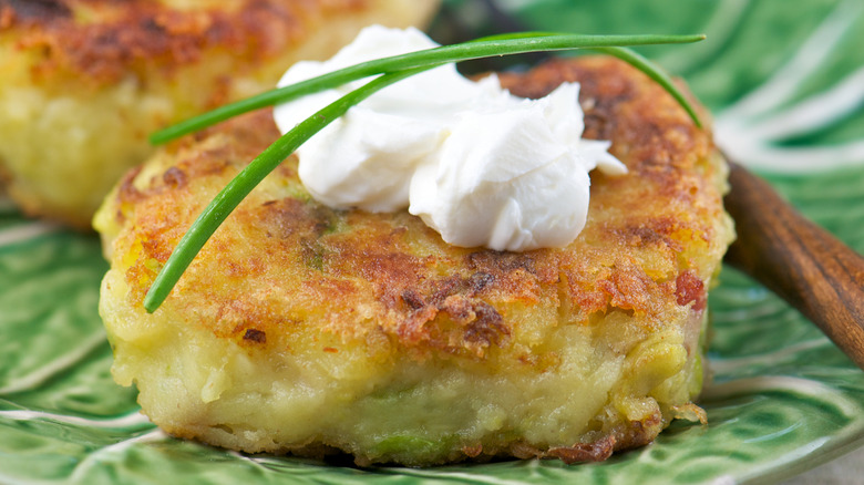 Close-up of fried potato cake with creme fraiche and chives on green plate