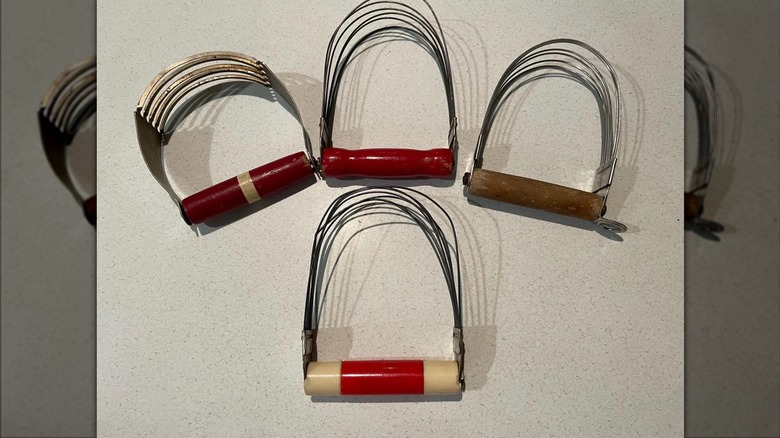 A green kitchen island with a vintage pastry cutter attached to the side, used to hold a colorful kitchen towel