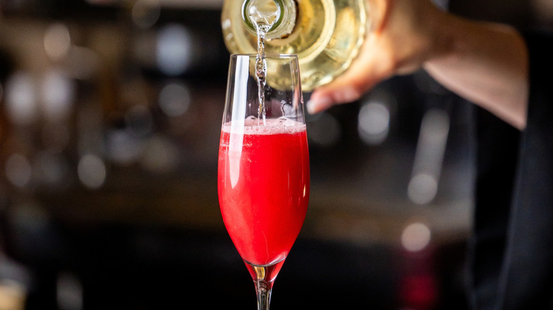 Bartender pouring champagne into a red drink.