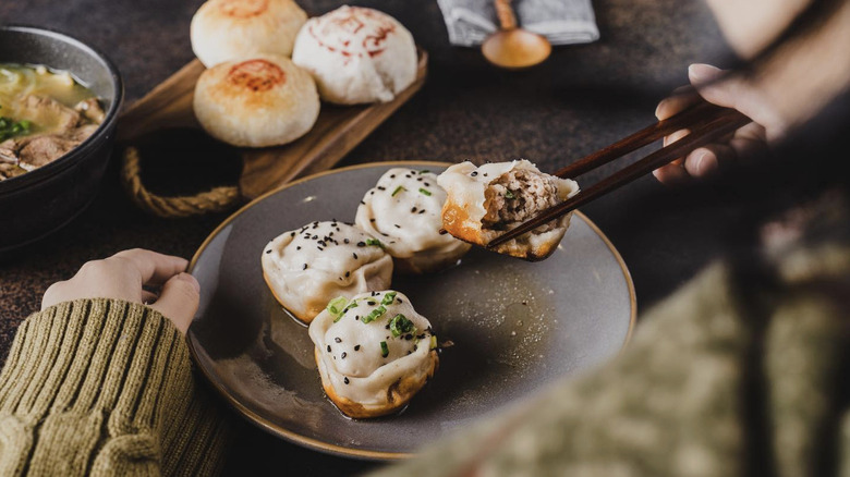 Someone using chopsticks to lift bao buns from a plate