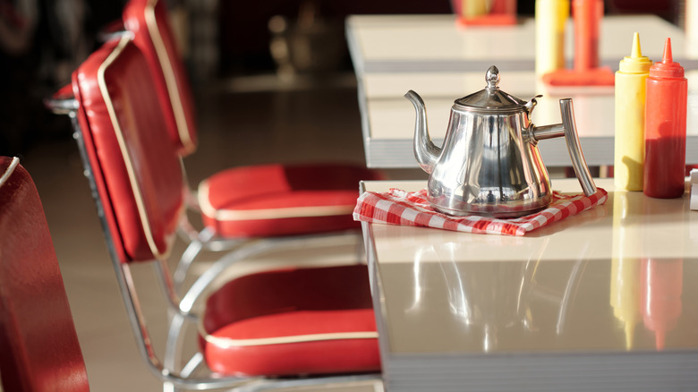 Interior of a retro diner with red leather chairs. Silver pitcher and condiment bottles are on the table.