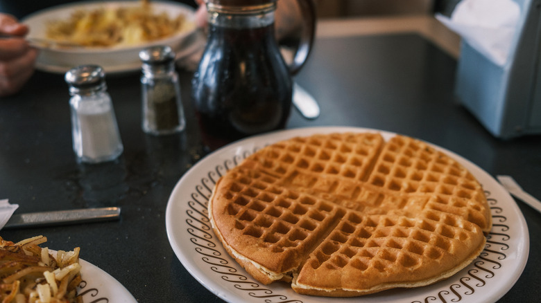 Large Waffle House waffle on a plate, with a pitcher of syrup in the background