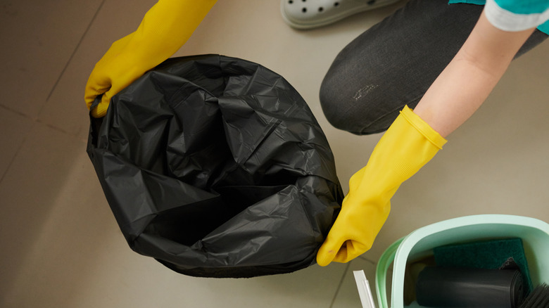 Someone wearing yellow gloves placing a garbage bag in a garbage can