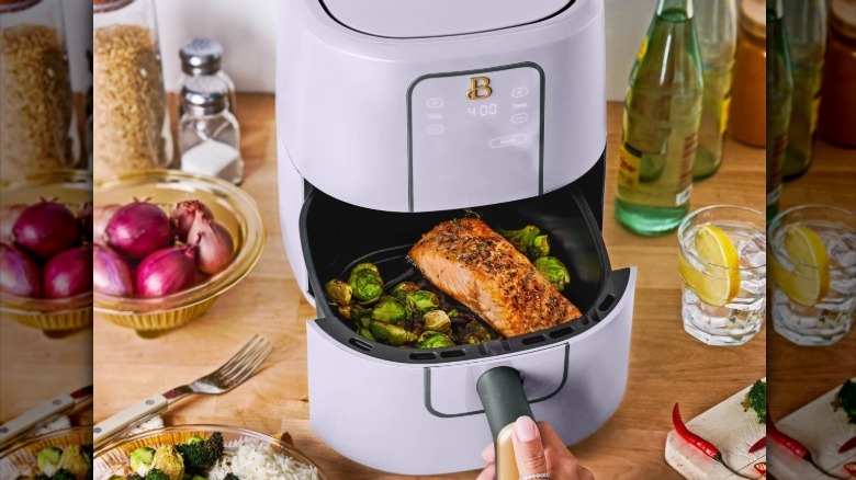 The 3-quart Beautiful by Drew air fryer in Lavender with the basket pulled out displaying cooked salmon and Brussels sprouts