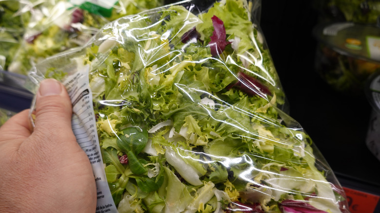 A person holding bagged salad