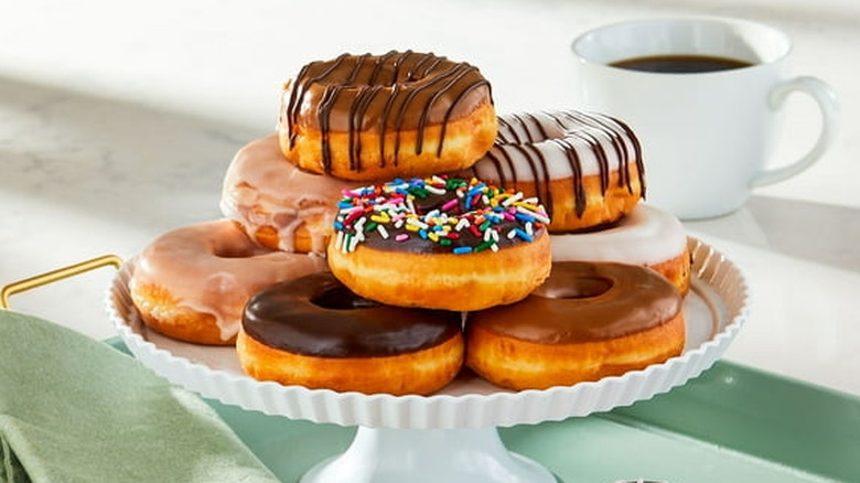 A platter of Walmart's colorful Freshness Guaranteed Assorted Ring Donuts on a table with a cup of coffee in the background