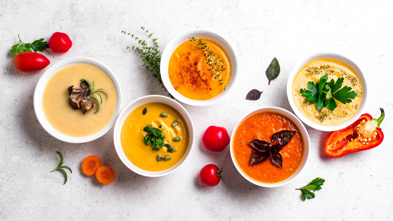 Various yellow and orange soups in white bowls with vegetable and herb garnishes