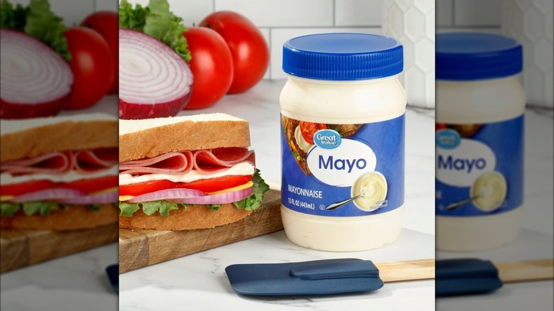 Jar of mayo beside sandwich, tomatoes, onion, and lettuce